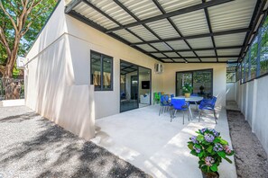 A covered outdoor area with a concrete floor, a table with chairs, and a potted plant.