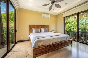 Quarto com cama grande, ventilador de teto e vista para o verde através da porta de correr.