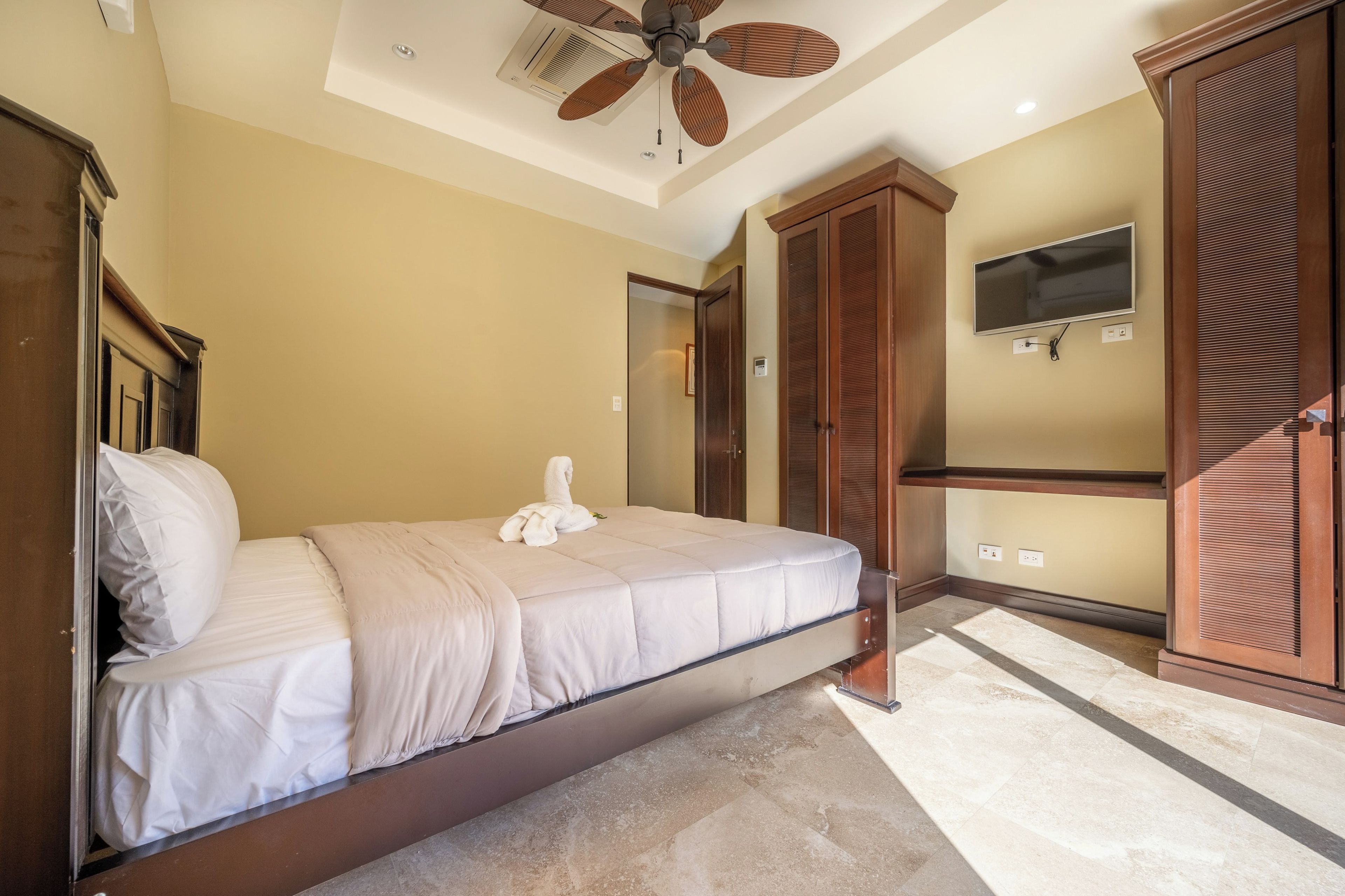 A bedroom with a bed, a ceiling fan, a TV, and a walk-in closet.