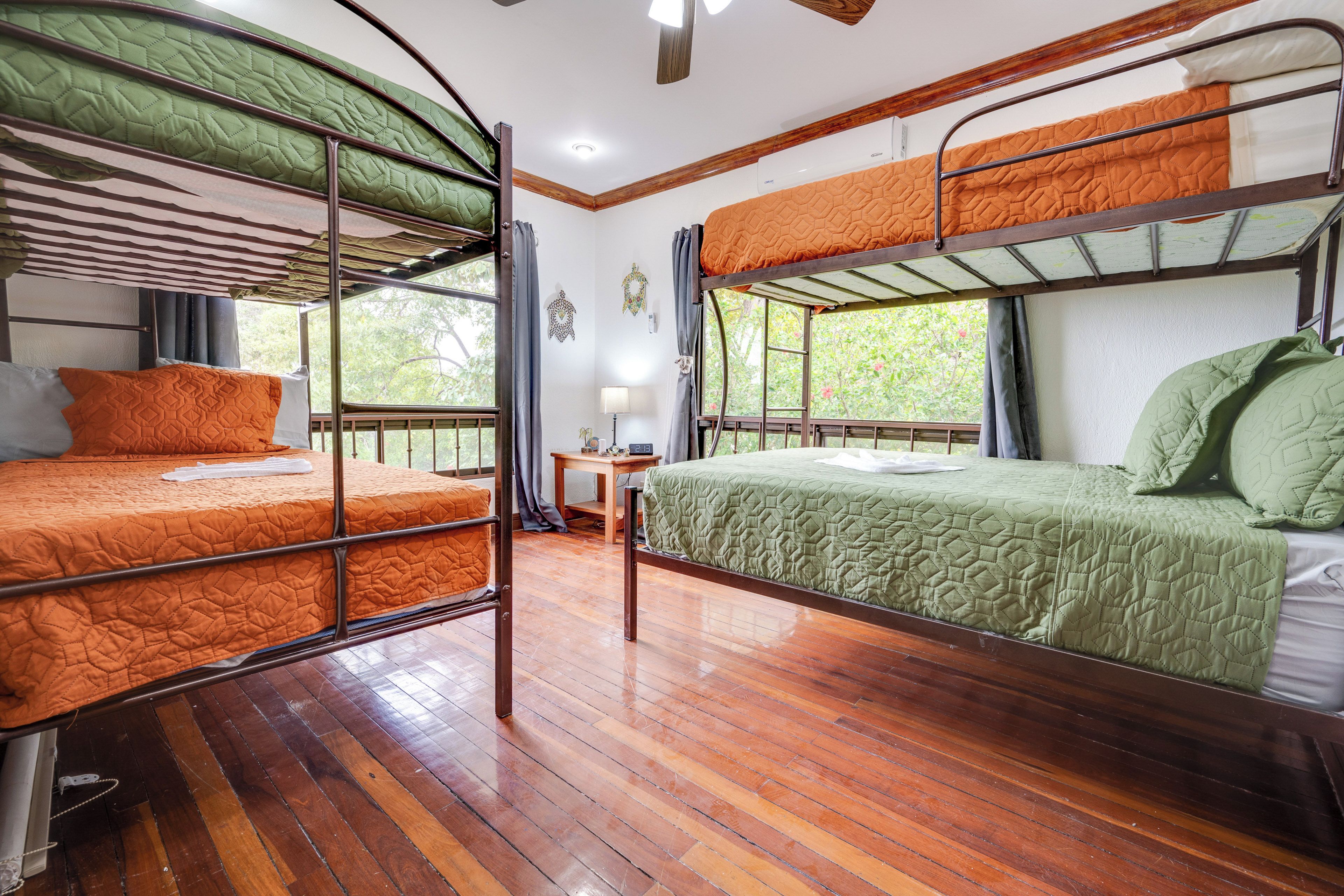 Un dormitorio con literas, suelo de madera, una mesita y una ventana con vistas a zonas verdes.