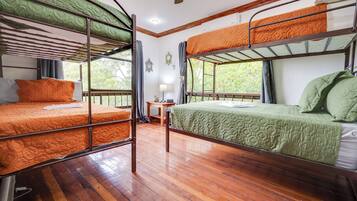 Un dormitorio con literas, suelo de madera, una mesita y una ventana con vistas a zonas verdes.