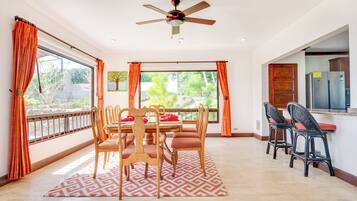 Un espace repas doté d’un ventilateur de plafond, d’une table à manger avec des chaises, et offrant une vue sur l’extérieur grâce à de grandes fenêtres.