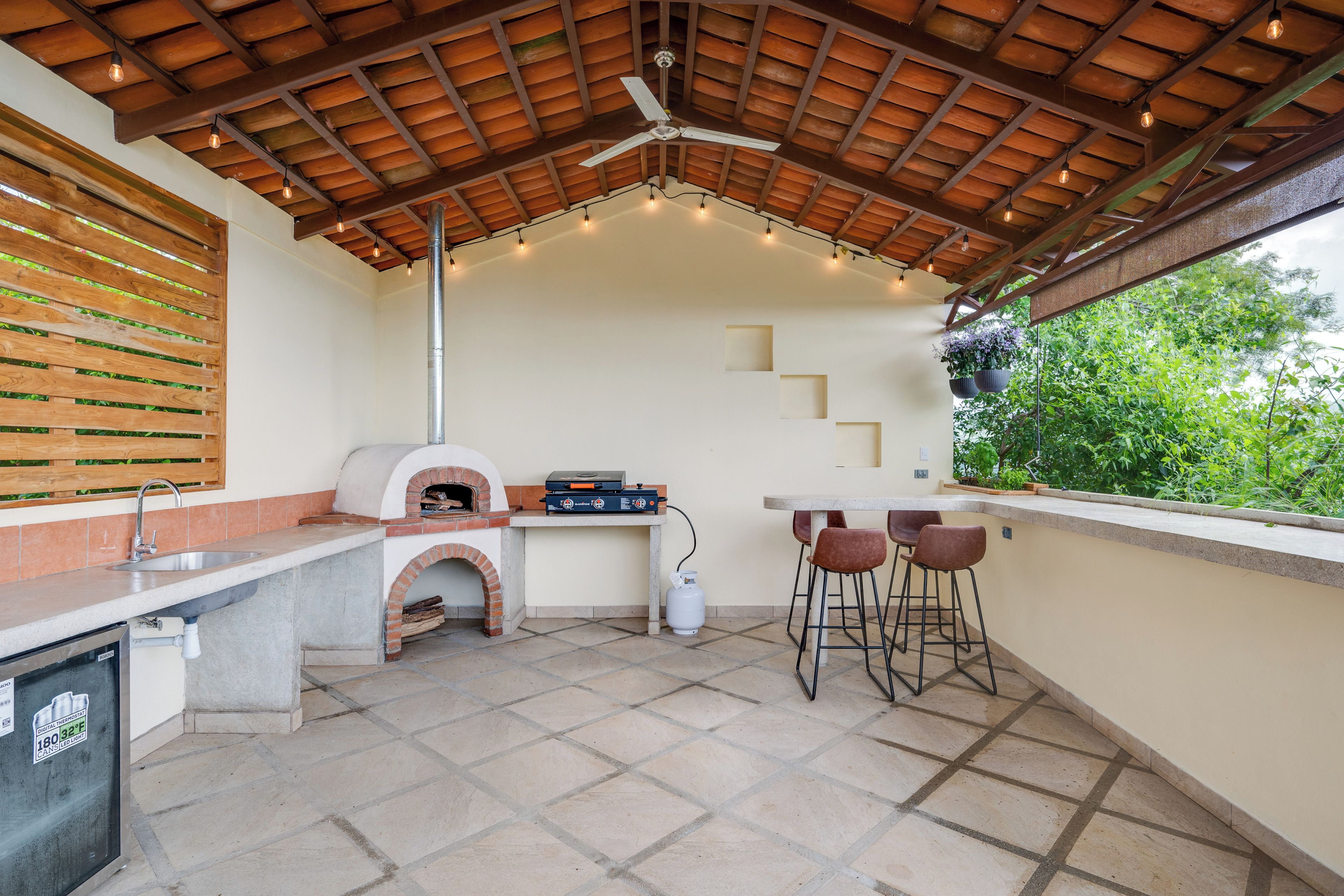 Un área de cocina al aire libre con horno de ladrillo, taburetes de bar y una mesa.