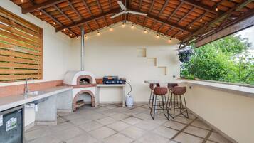 Un área de cocina al aire libre con horno de ladrillo, taburetes de bar y una mesa.