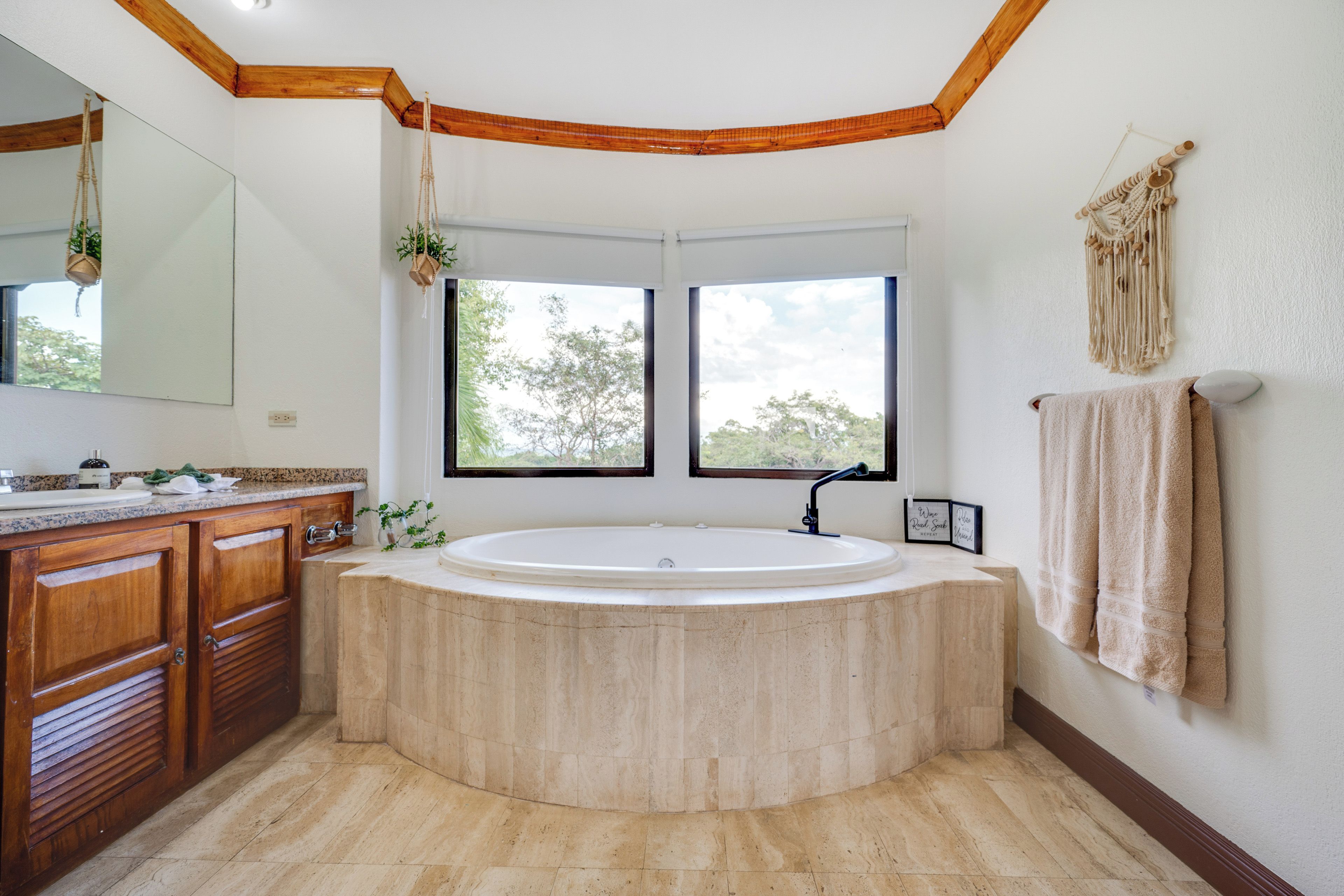Une salle de bain avec une baignoire sur pieds, des meubles en bois, un grand miroir et une décoration murale en macramé.
