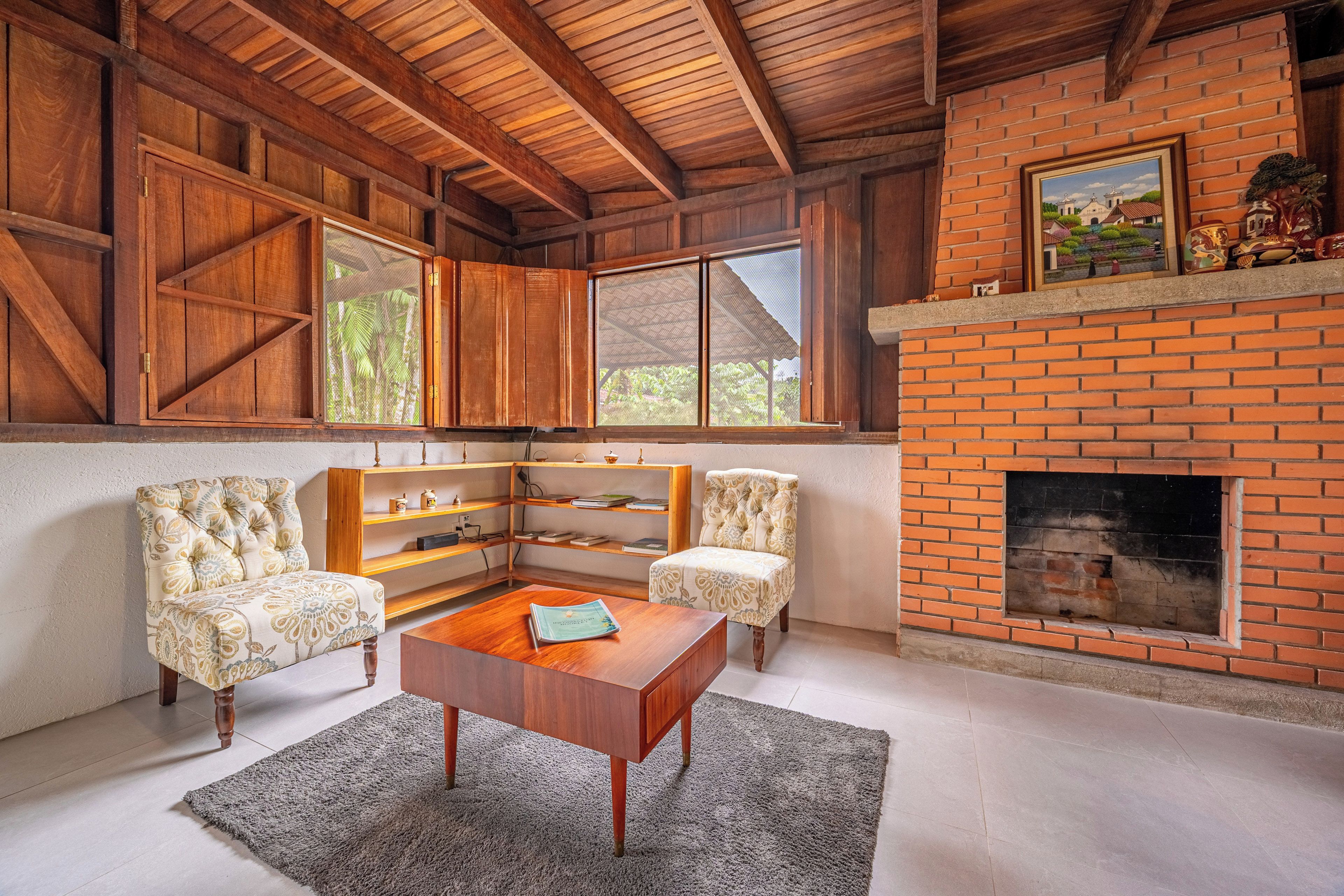 A cozy living room with a fireplace, wooden beams, and a view of greenery outside.