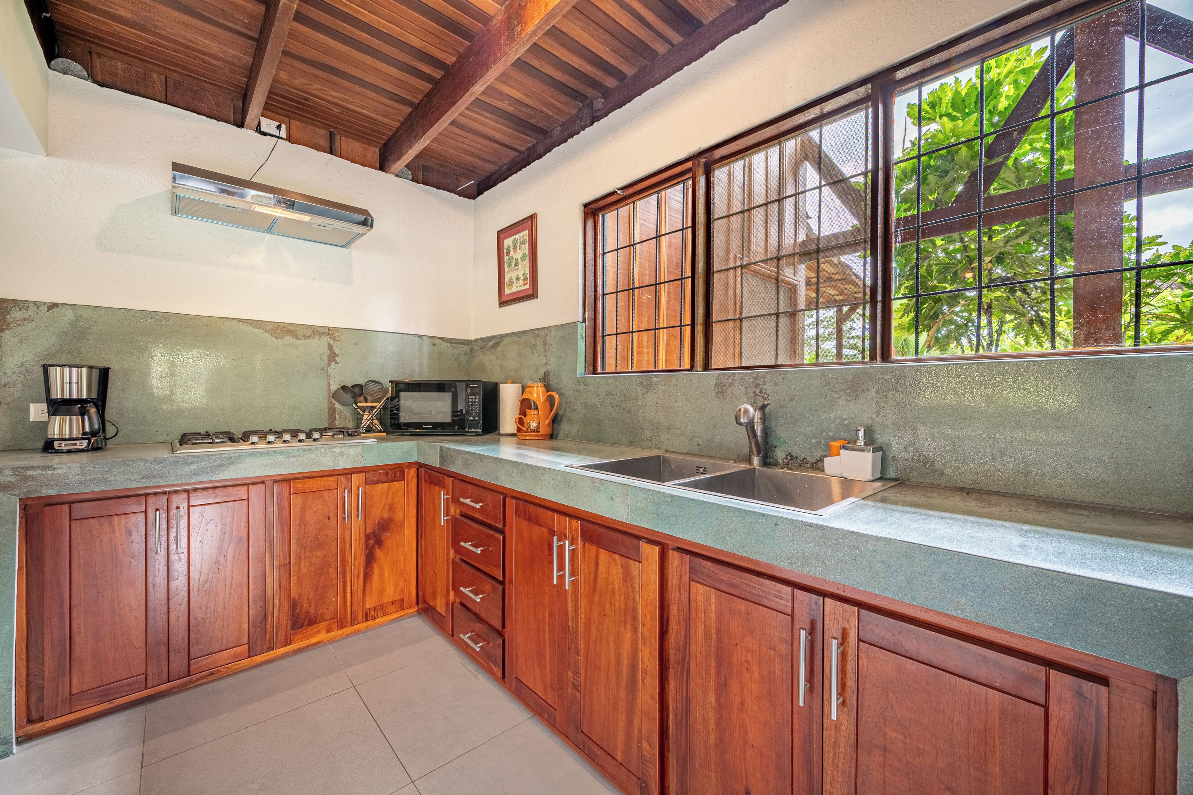 A kitchen with wooden cabinets, a microwave, a coffee maker, and a large window with a view of greenery.