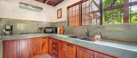 A kitchen with wooden cabinets, a microwave, a coffee maker, and a large window with a view of greenery.
