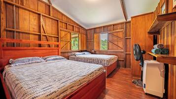 A room with two beds, wooden walls, a fan, and a small refrigerator.