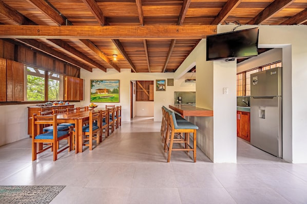 A spacious kitchen with wooden cabinets, a dining area with a long table and chairs, and a large TV mounted on the wall.