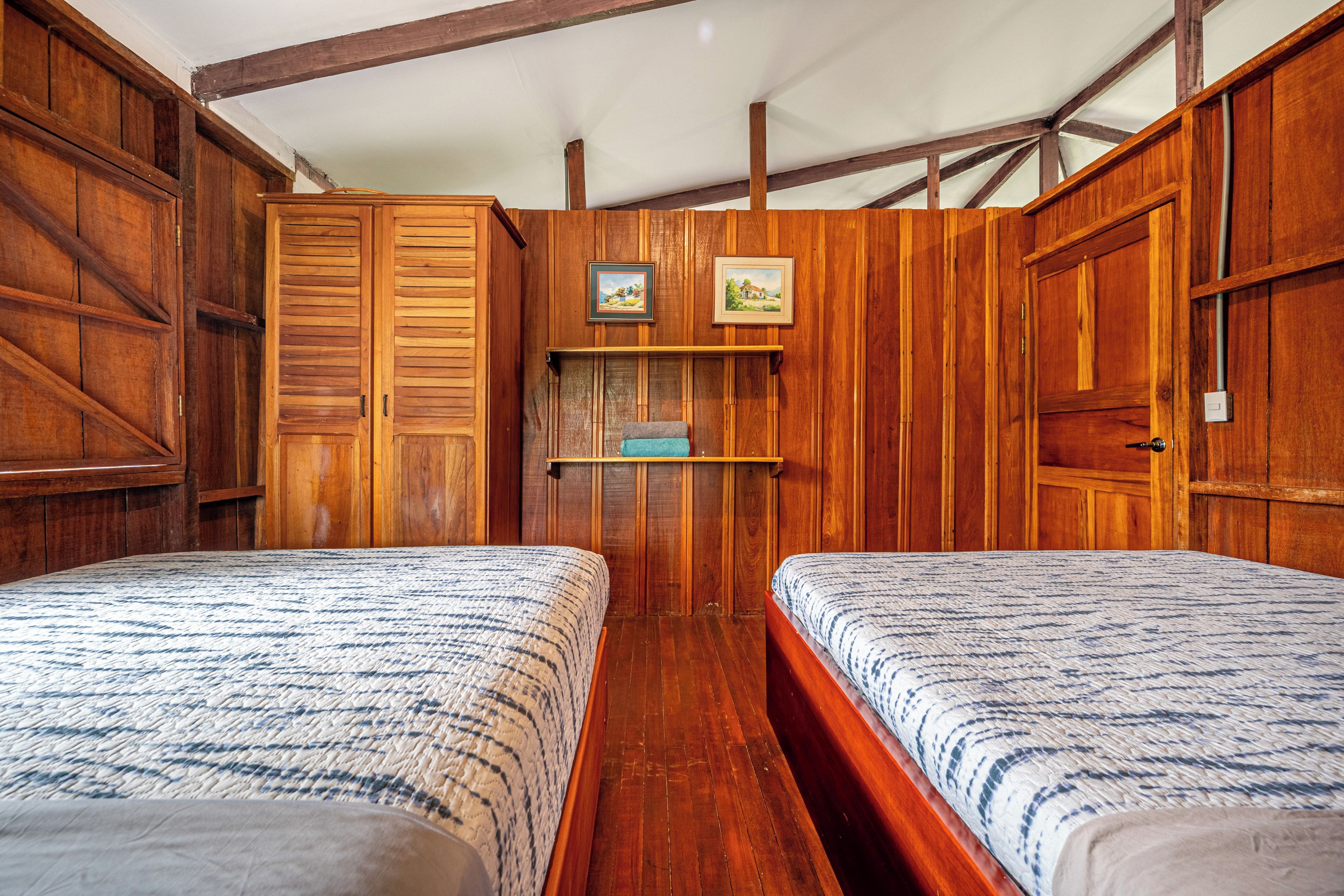 A room with two beds, wooden walls, and a shelf with pictures.