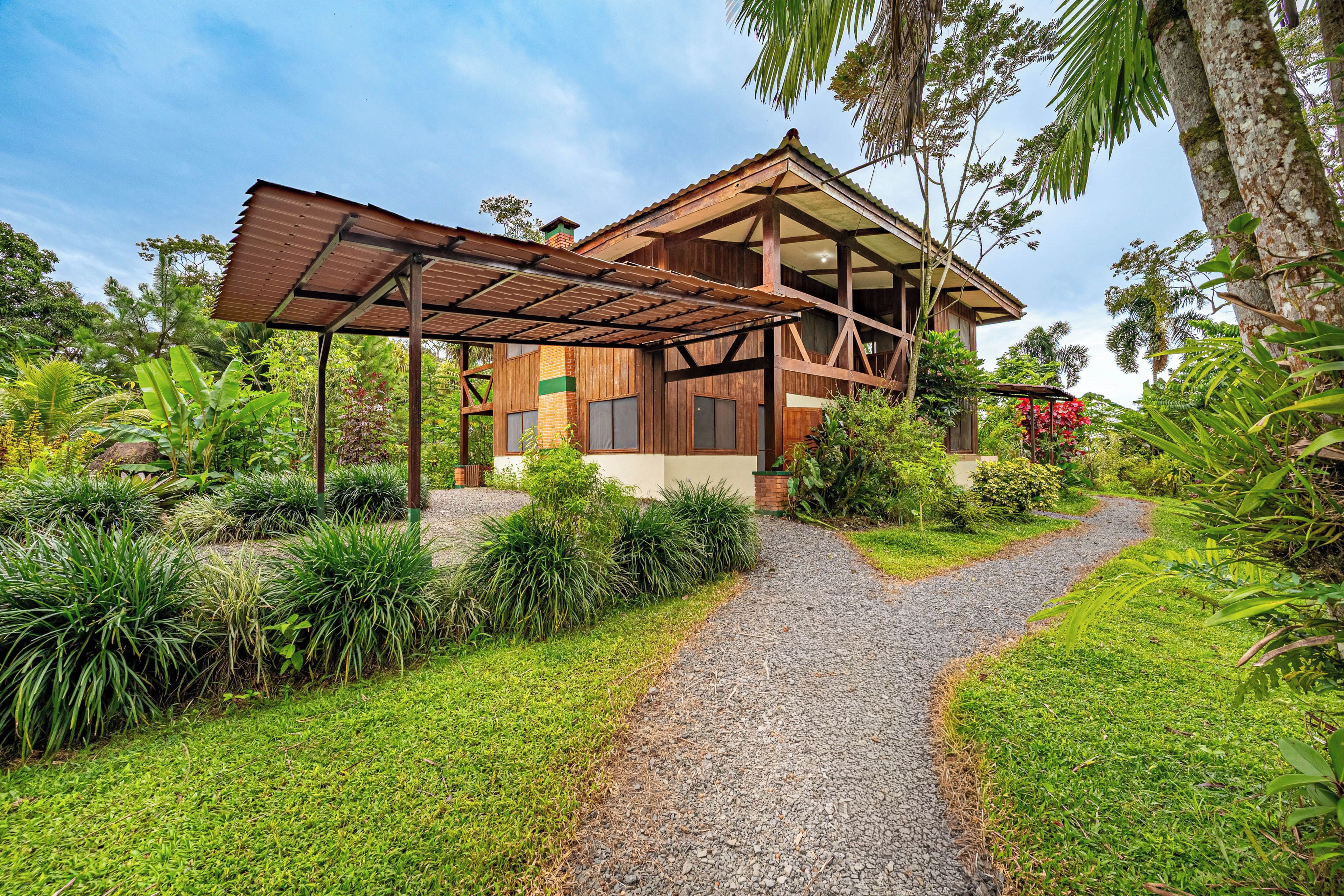 A wooden house with a gravel pathway leading to it, surrounded by lush greenery.