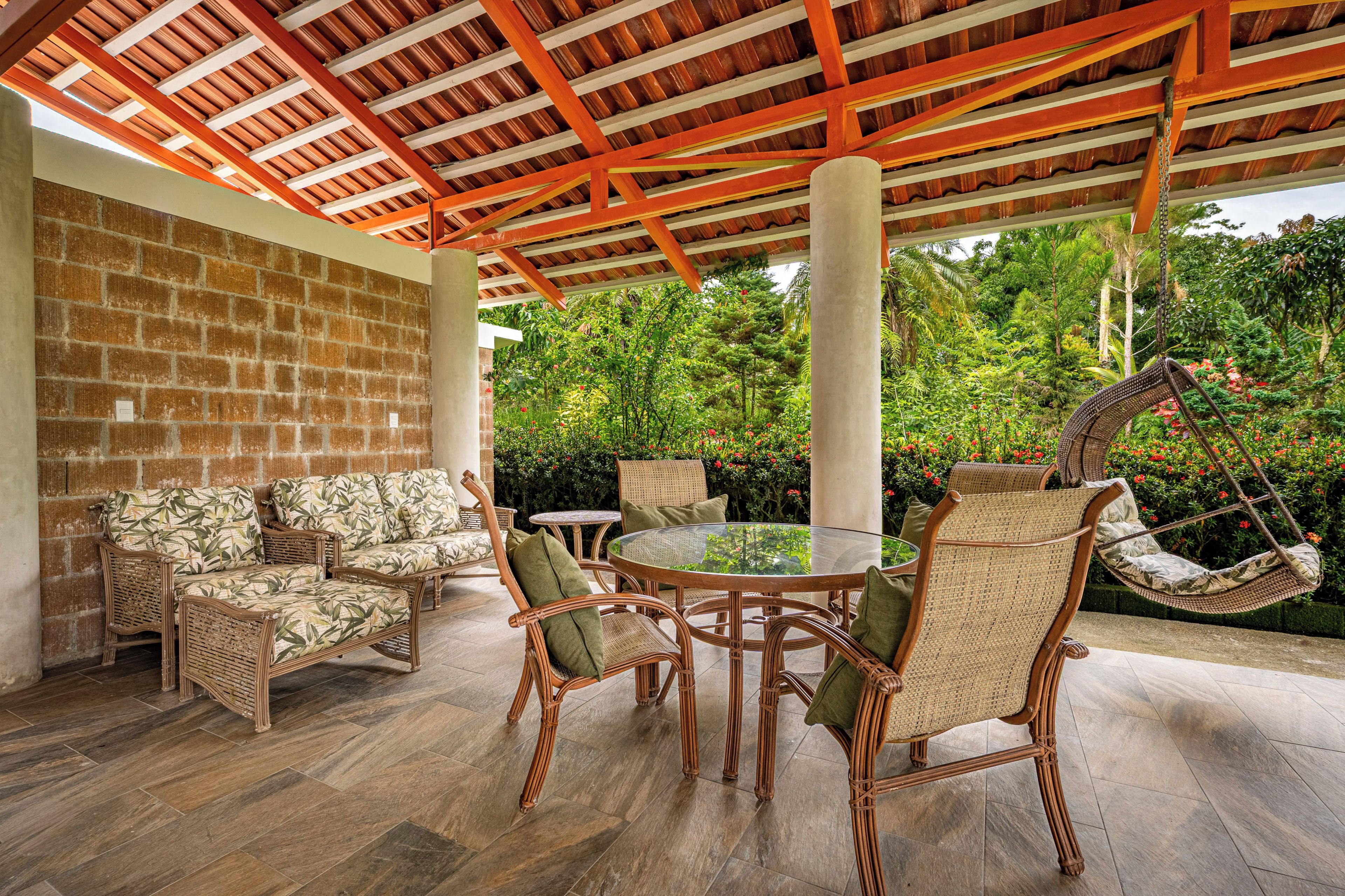 A covered outdoor seating area with wicker furniture and a glass table.