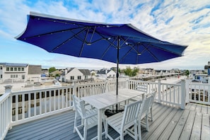 A wooden deck with a table and chairs, a blue umbrella, and a view of a residential area with houses and a body of water.