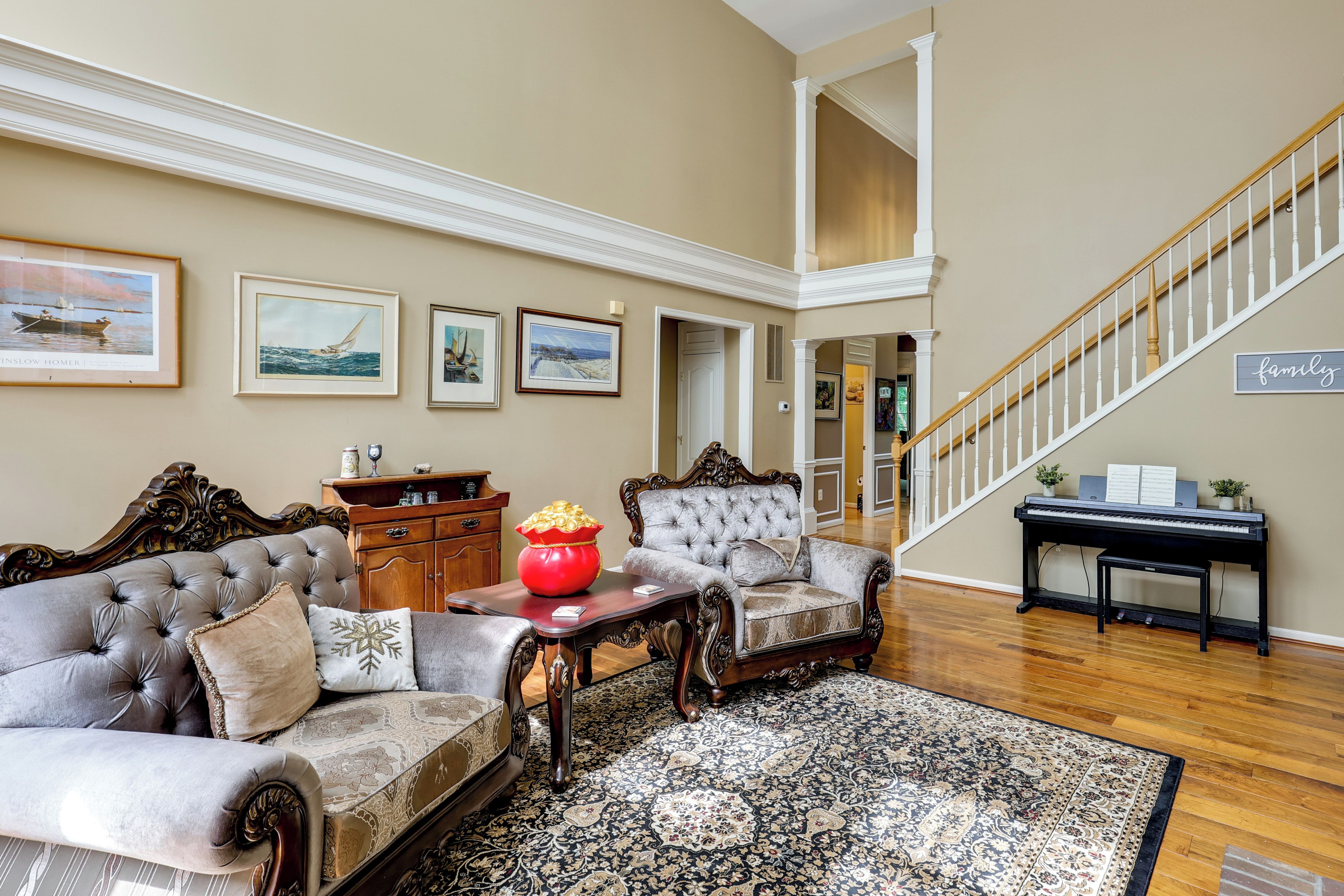 A spacious living room with a grand staircase, elegant furniture, and artwork on the walls.