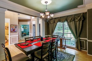 A dining area with a table set for four, a chandelier, and a view of the outdoors through a window. - Walk to Herrington Harbor: Spacious Bay Home (Tracys Landing)