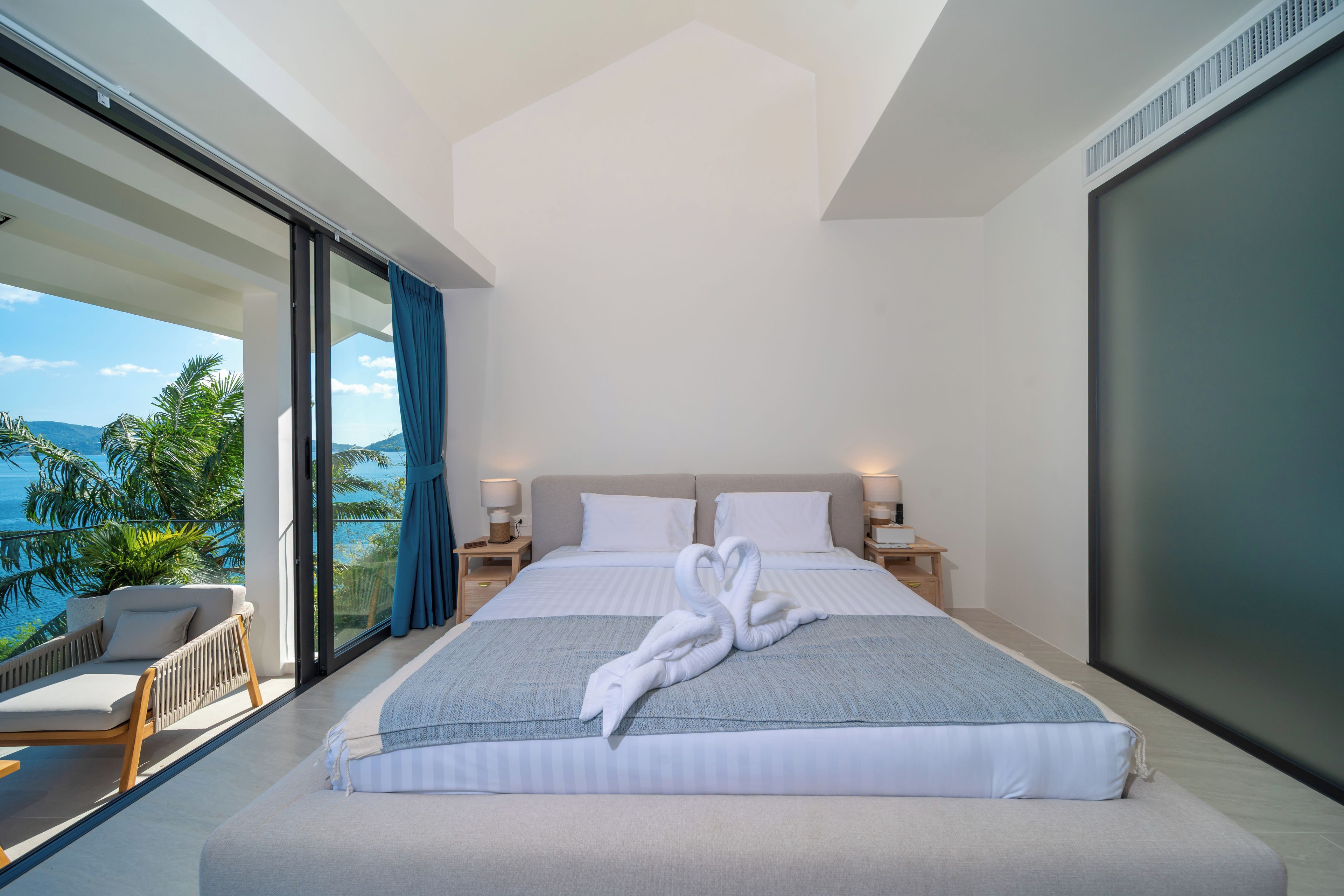 Una habitación de hotel moderna con una cama grande, vistas al mar y un balcón con una silla.
