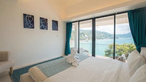 A hotel room with a bed, a chair, a view of the sea, and three abstract paintings on the wall. - Villa SARA (Kathu)