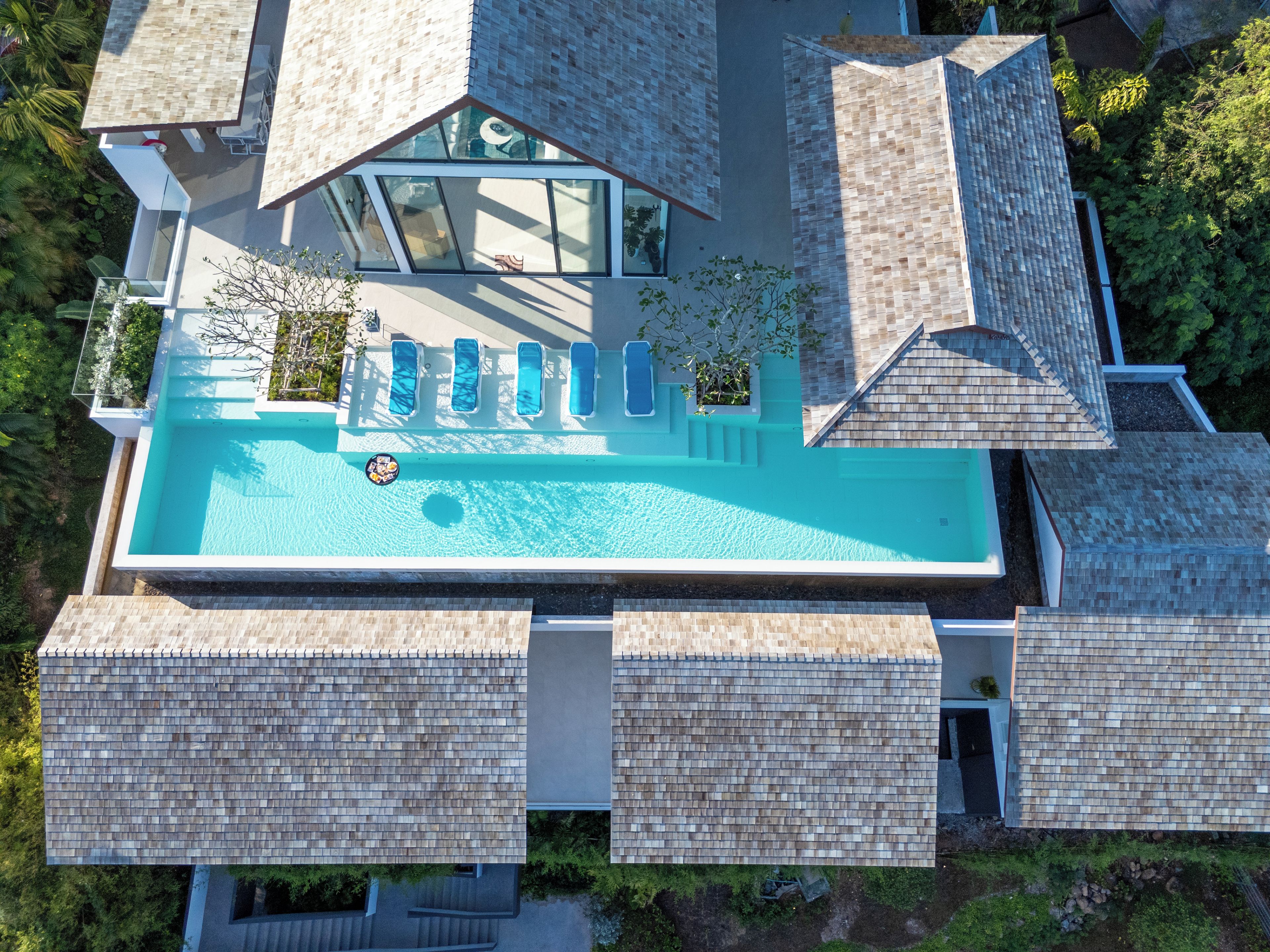 Vista aérea de uma casa moderna com piscina, várias plataformas e uma grande janela de vidro.