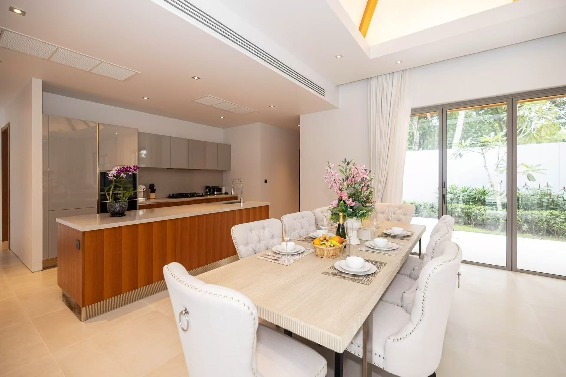 Un comedor moderno con una mesa de madera, sillas blancas tapizadas y una cocina al fondo.