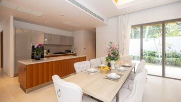 Un comedor moderno con una mesa de madera, sillas blancas tapizadas y una cocina al fondo.