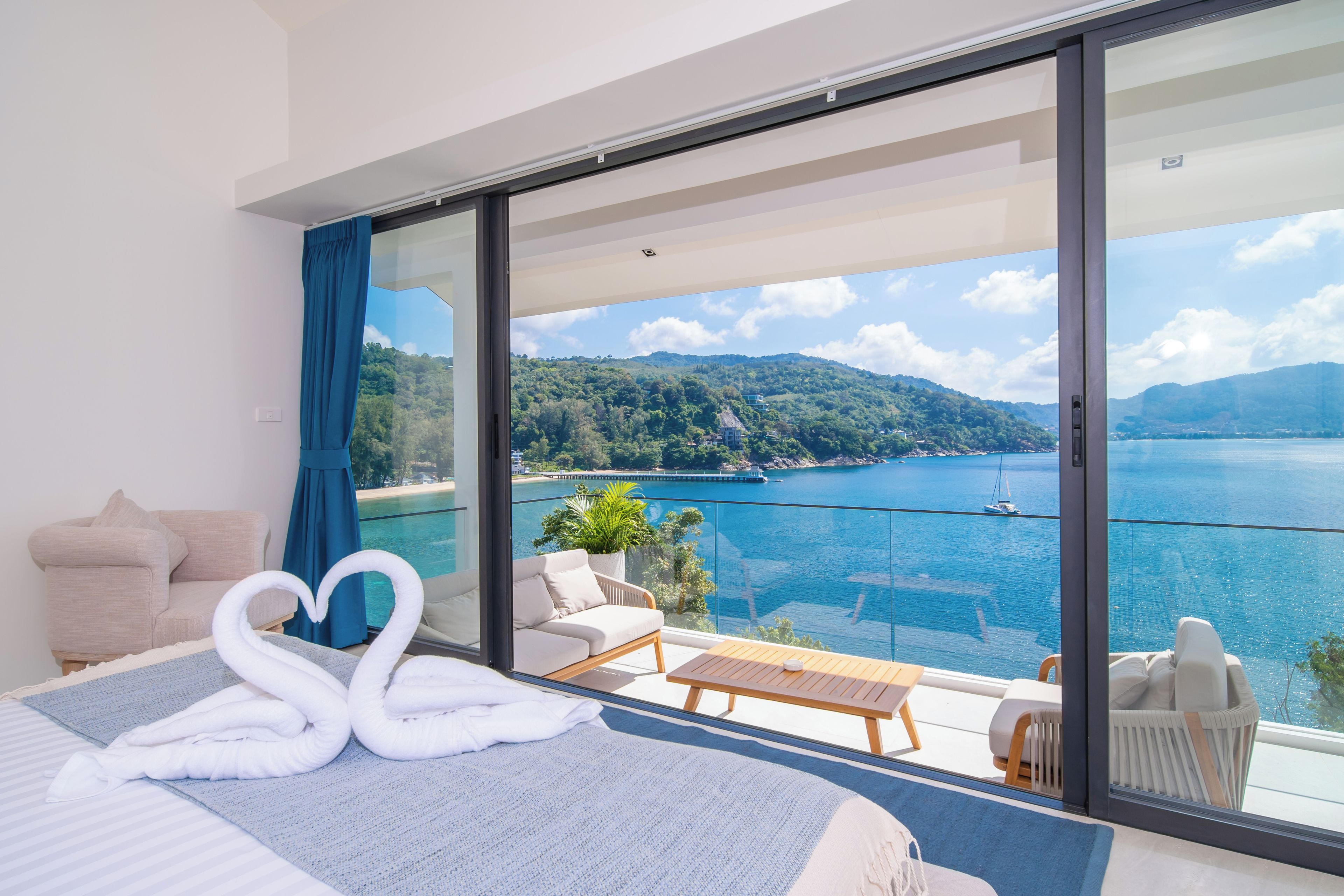 Habitación de hotel con cama, sofá, balcón y vistas a un lago y montañas.