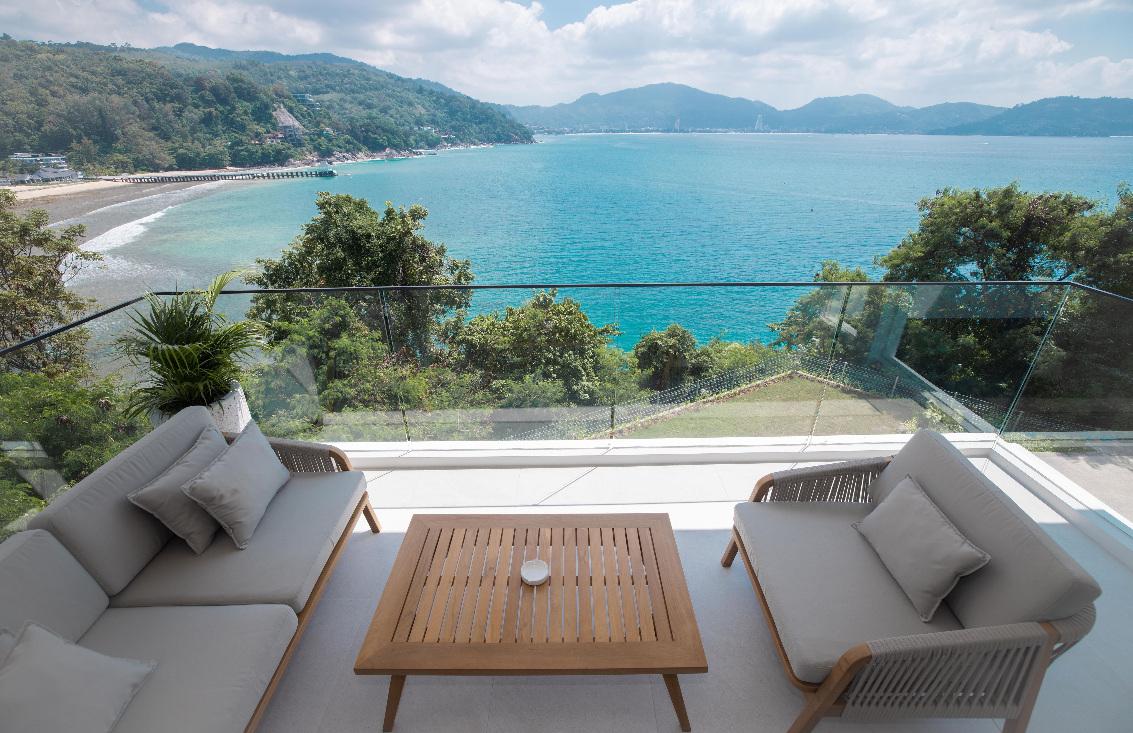 Un balcon avec vue sur une plage et la mer. On y voit deux canapés et une table au premier plan.