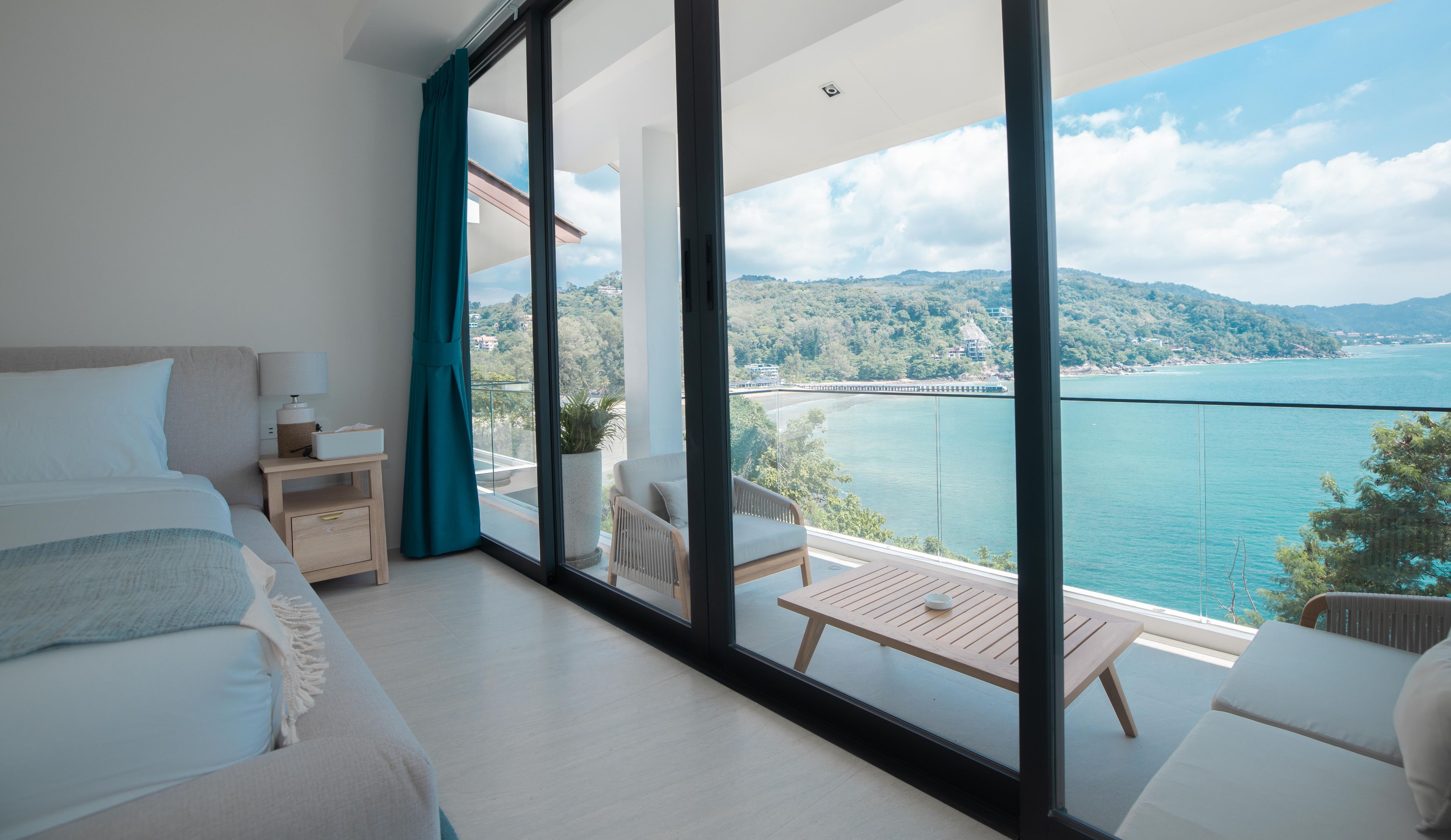 Un dormitorio moderno con un ventanal grande, una cama, una mesita de noche y vistas a un lago y montañas.