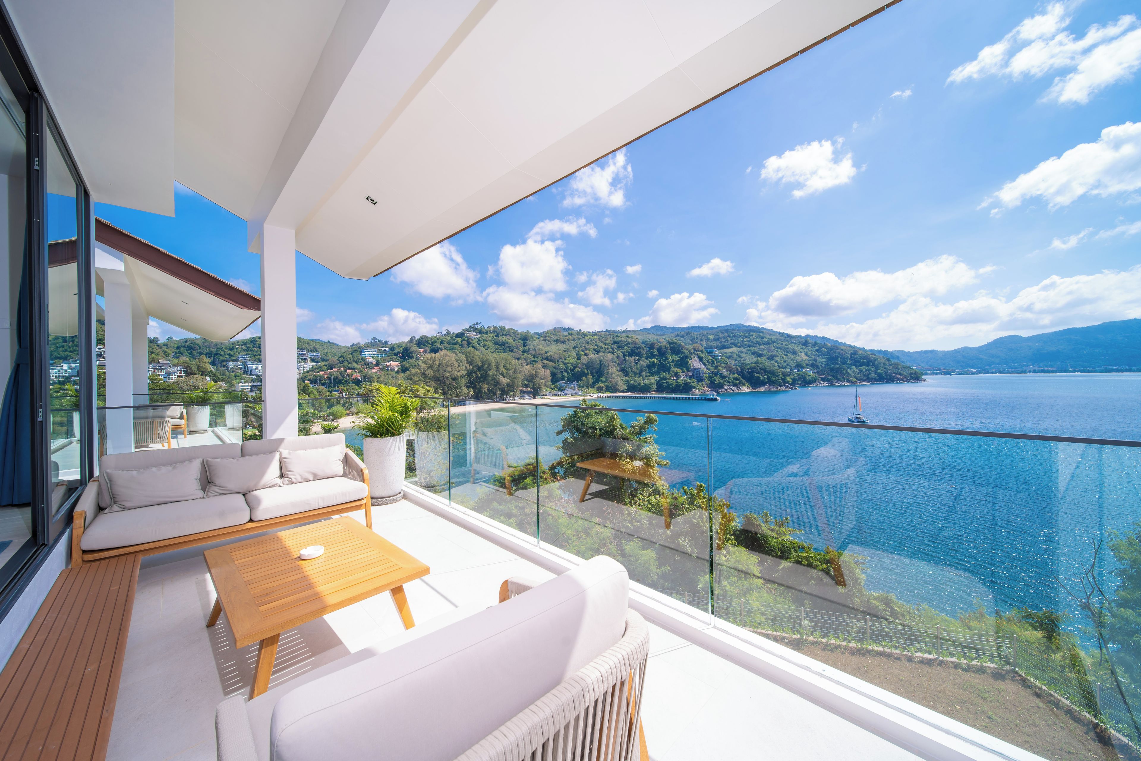 A balcony with a view of a lake and mountains, furnished with a sofa, table, and chairs.