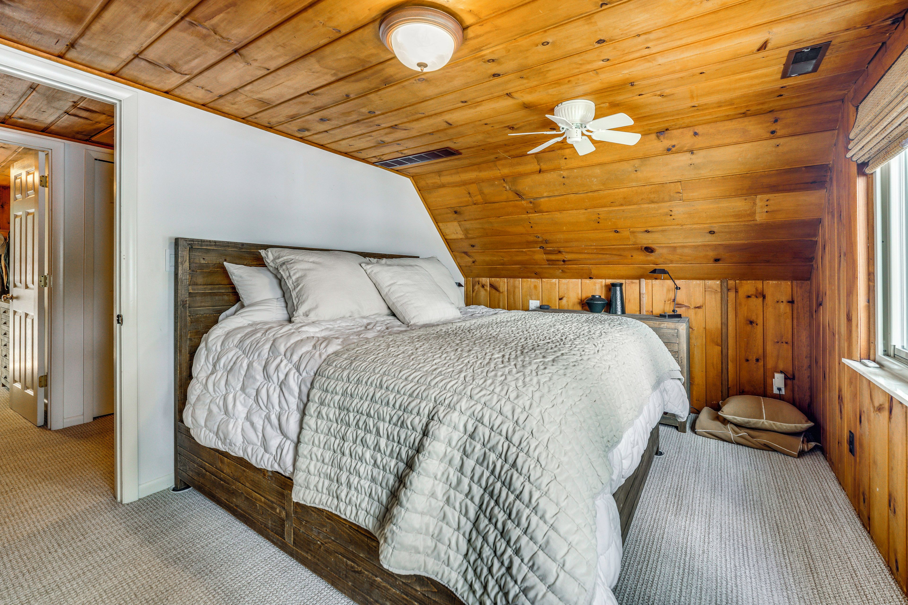 A bedroom with a wooden ceiling, a bed with a quilt, a ceiling fan, and a window.