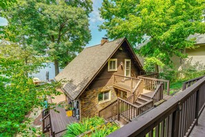 A wooden cabin with a stone foundation, a wooden deck, and a staircase leading to the entrance.