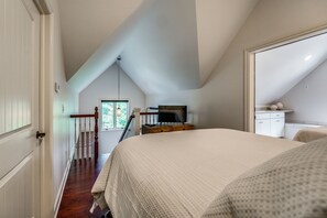 A bedroom with a large bed, a wooden dresser, a television, and a window with a view of trees.