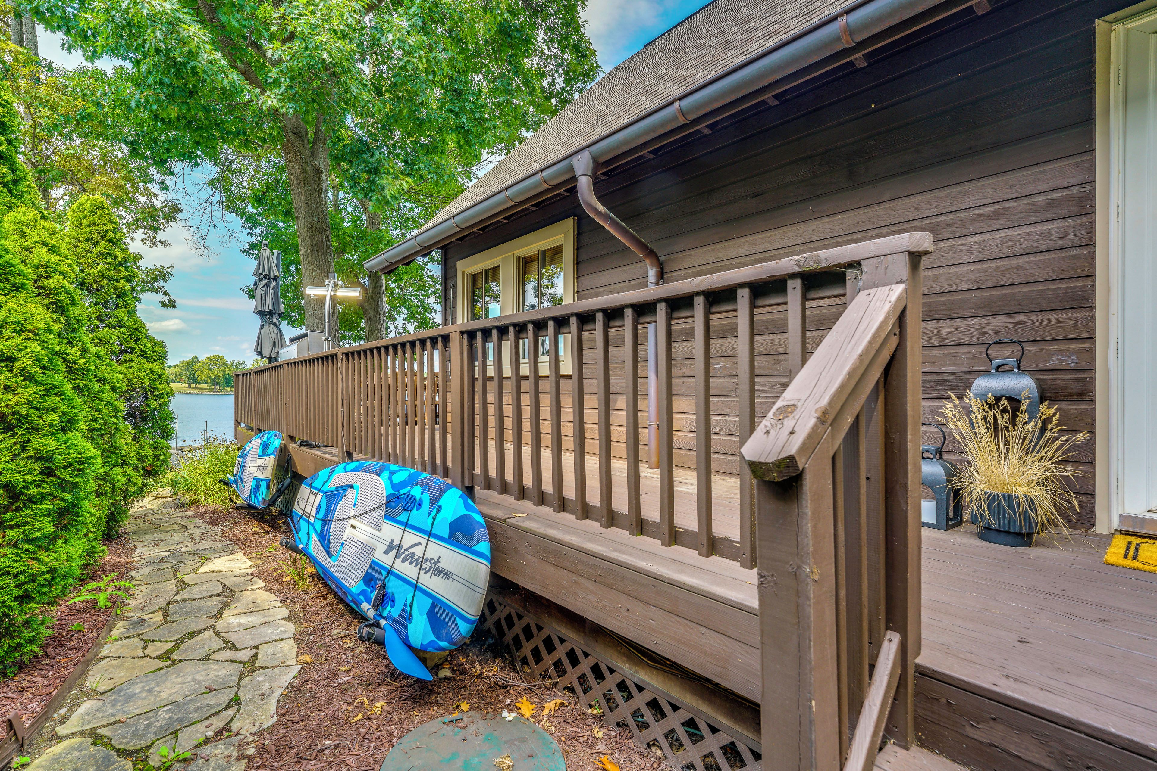 A wooden deck with a railing, a stone pathway, and a body of water in the background.