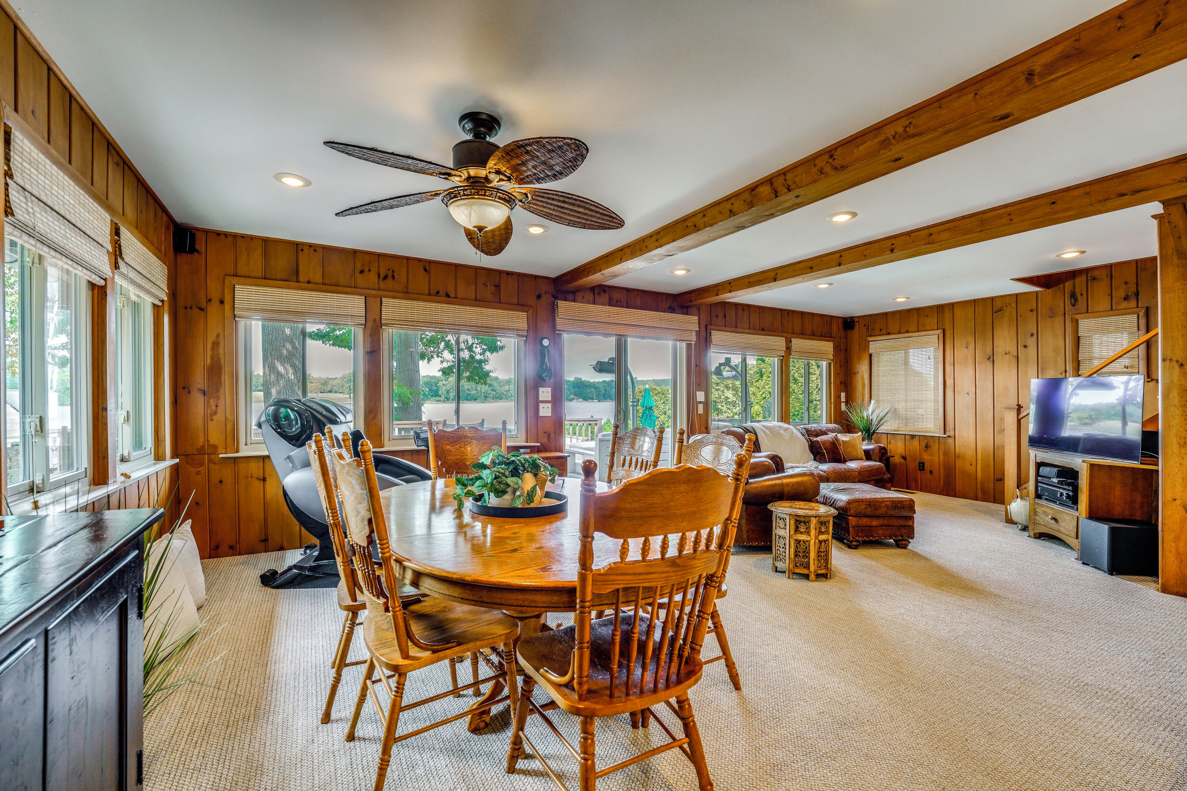 A spacious room with a dining table, chairs, a ceiling fan, and a television.