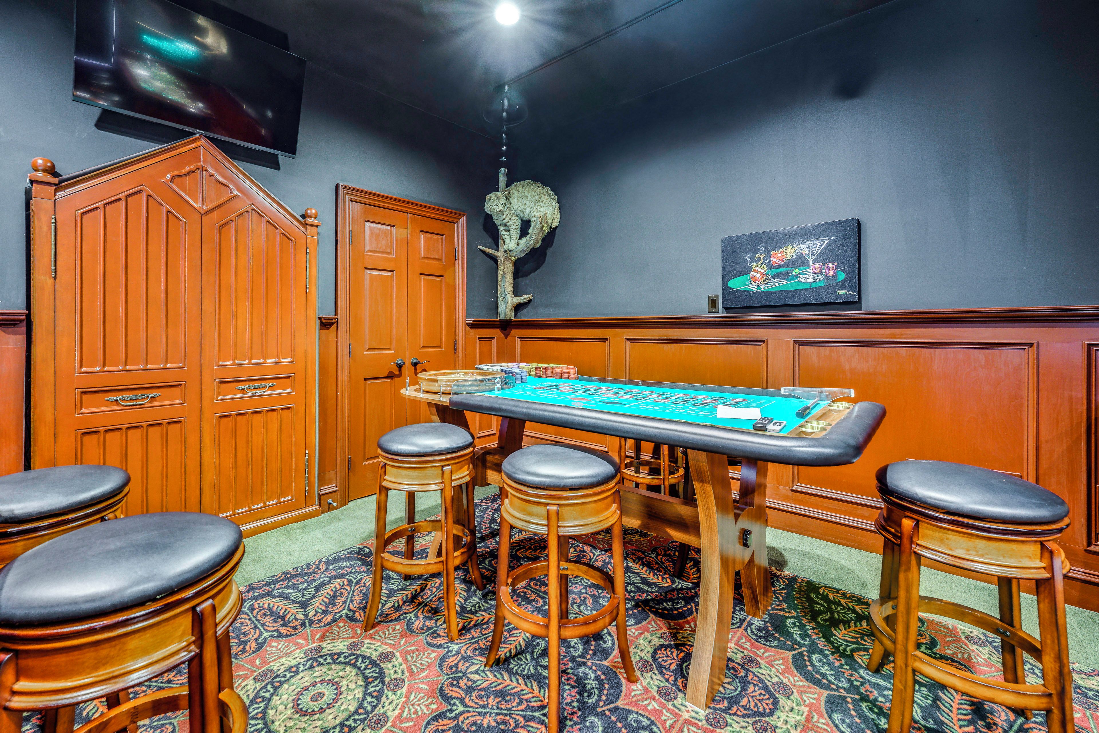 Une pièce comprenant une table de craps, des tabourets de bar en bois, un téléviseur et un élément décoratif mural.