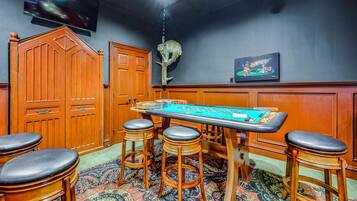 A room with a craps table, wooden bar stools, a television, and a decorative wall piece.