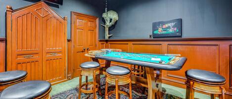 Une pièce comprenant une table de craps, des tabourets de bar en bois, un téléviseur et un élément décoratif mural.