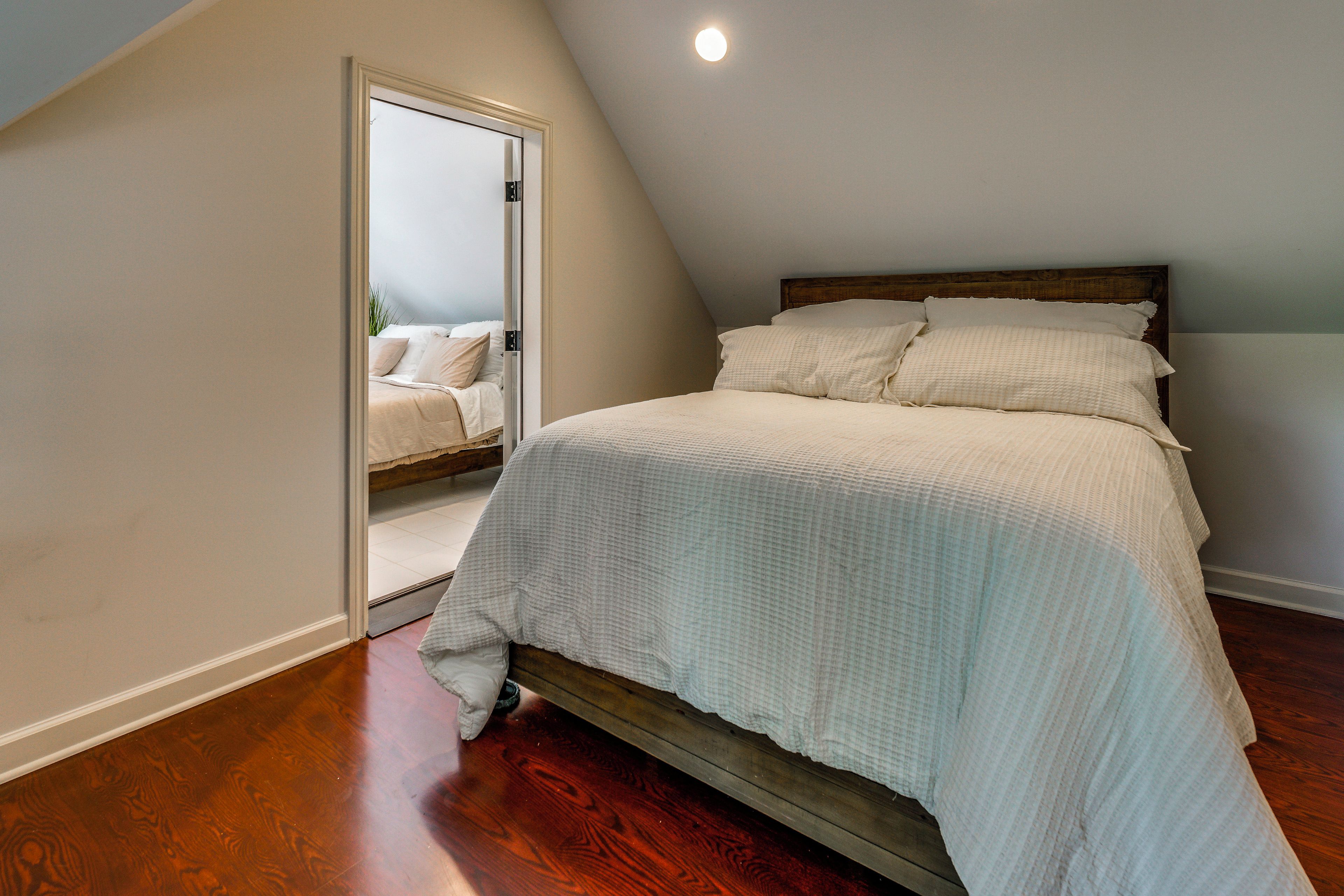 A bedroom with a bed, wooden floor, and a door leading to another room.