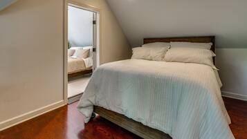 A bedroom with a bed, wooden floor, and a door leading to another room.