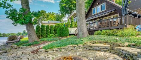 A lakeside cabin with a stone fire pit, a wooden deck, and a view of the lake.