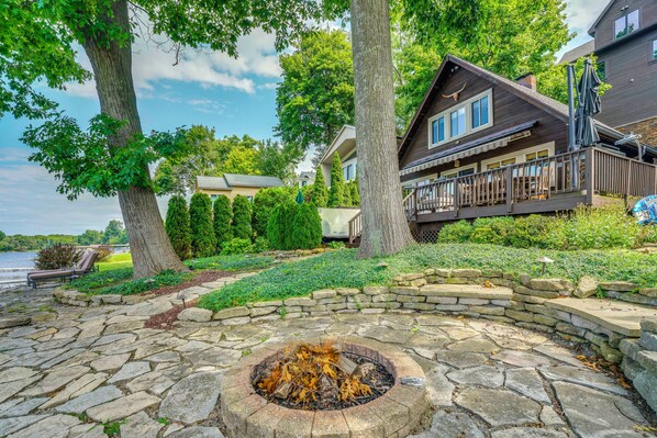 A lakeside cabin with a stone fire pit, a wooden deck, and a view of the lake.