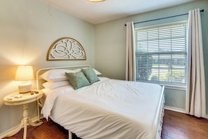 Une chambre à coucher avec un lit, une table de chevet avec une lampe, un élément décoratif mural et une fenêtre avec des rideaux.