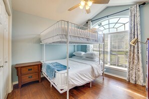 A bunk bed with a wooden nightstand and a window with blinds.