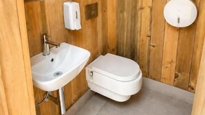 A wooden-paneled bathroom with a white sink, toilet, and a towel dispenser. - La Ballenera Lodge (La Ballena)