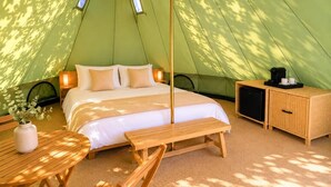 A tent with a bed, bedside table, bench, and a small cabinet. - La Ballenera Lodge (La Ballena)