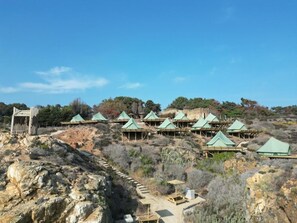 A series of wooden cabins with green roofs, arranged on a hillside with a clear sky above.
