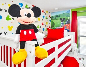 Ein Kinderzimmer mit einem Mickey Mouse Stofftier auf einem weißen Etagenbett mit roter Bettwäsche.