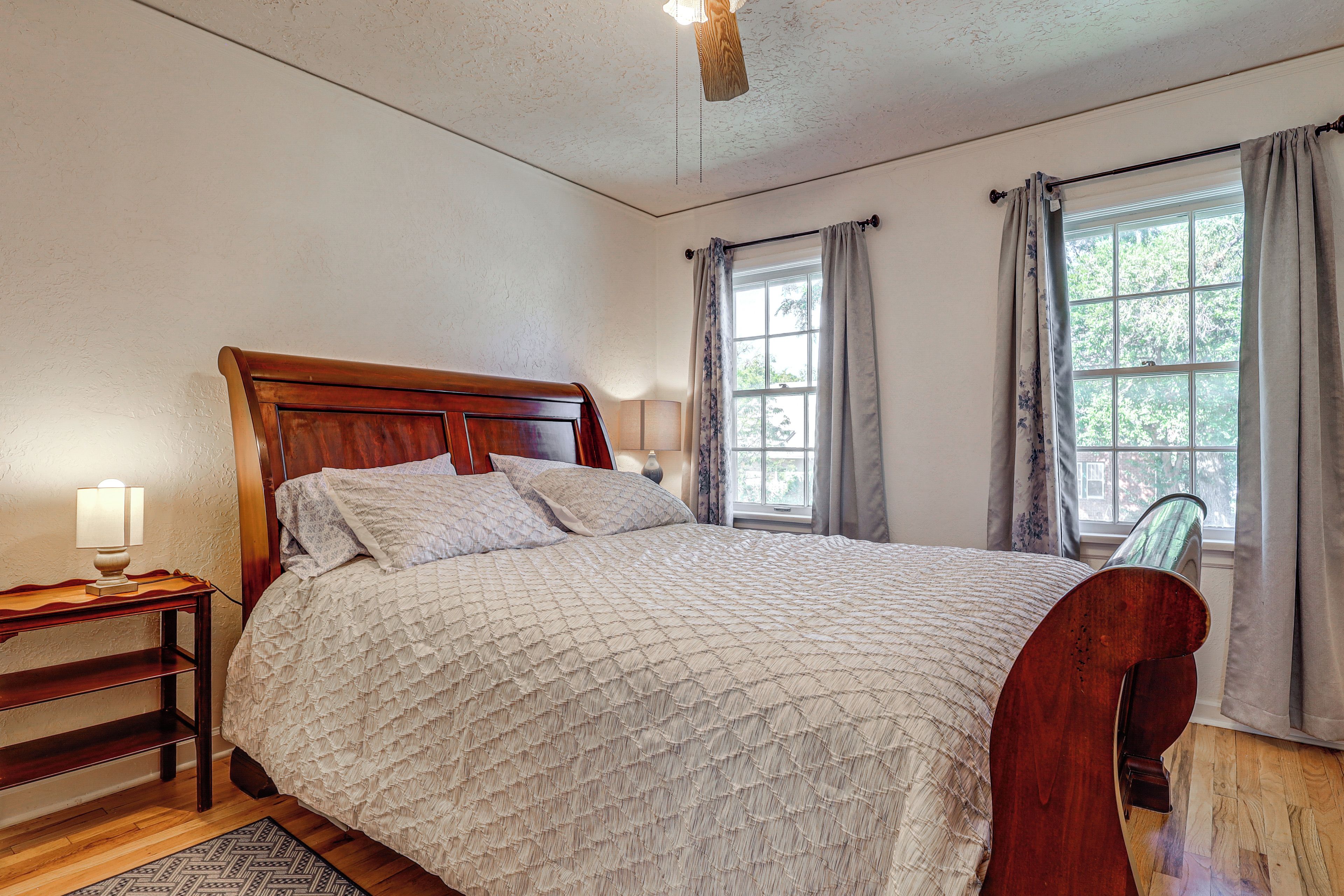 Un dormitorio con una cama de madera, una mesita de noche, una lámpara y una ventana con cortinas.
