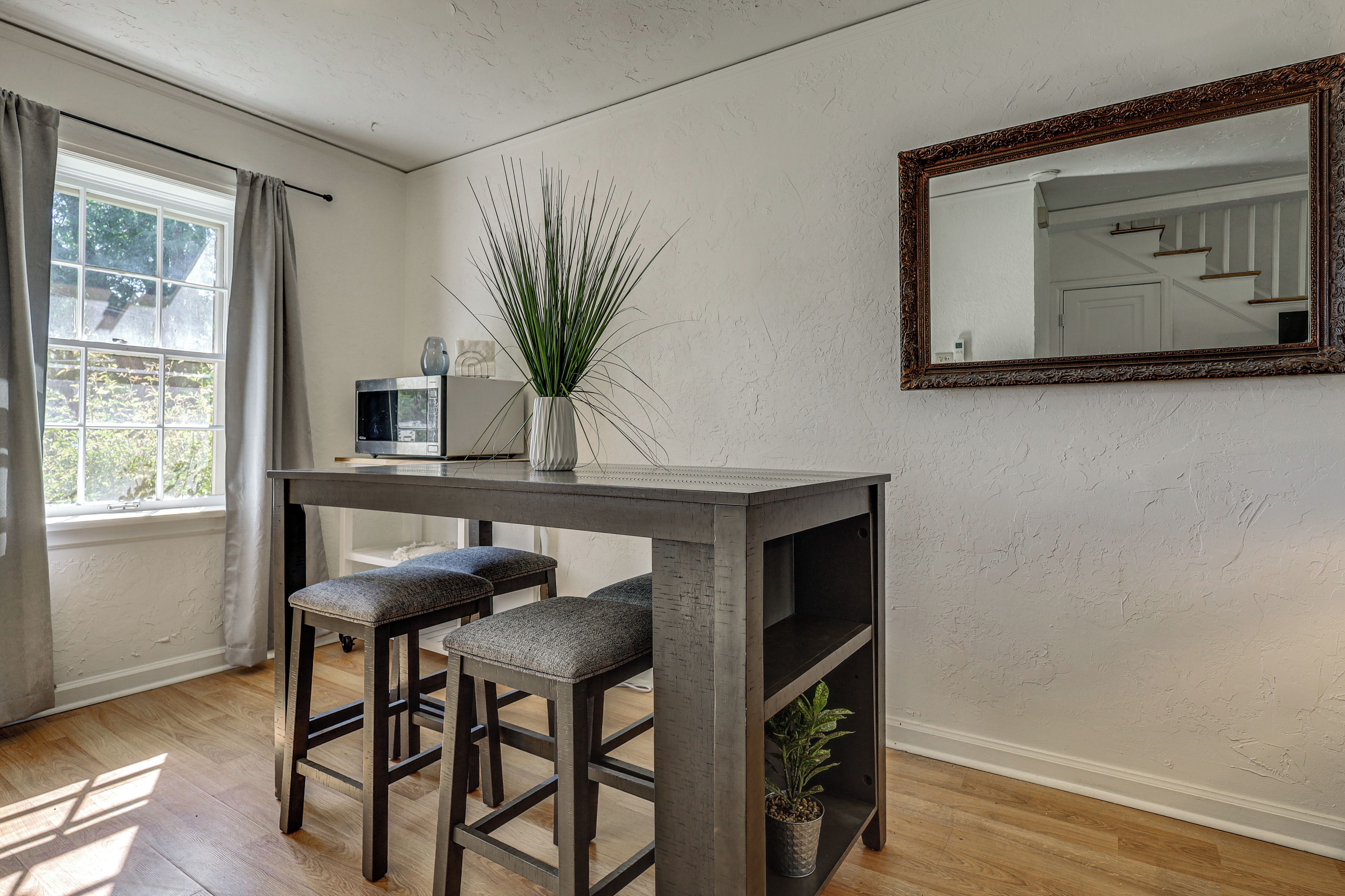 A room with a wooden table, two barstools, a potted plant, a television, and a mirror on the wall.