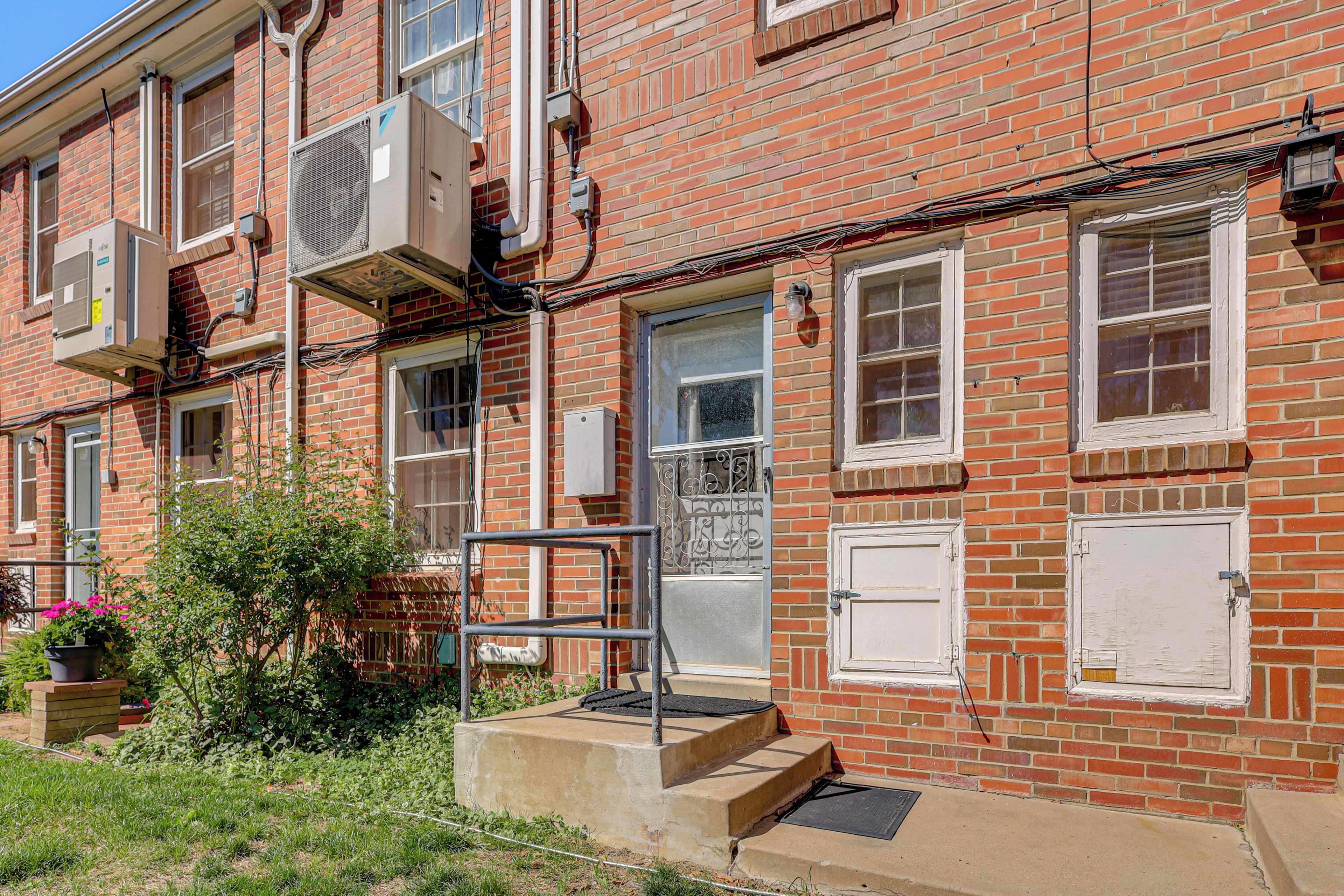 A red brick building with multiple windows, a door, and air conditioning units.